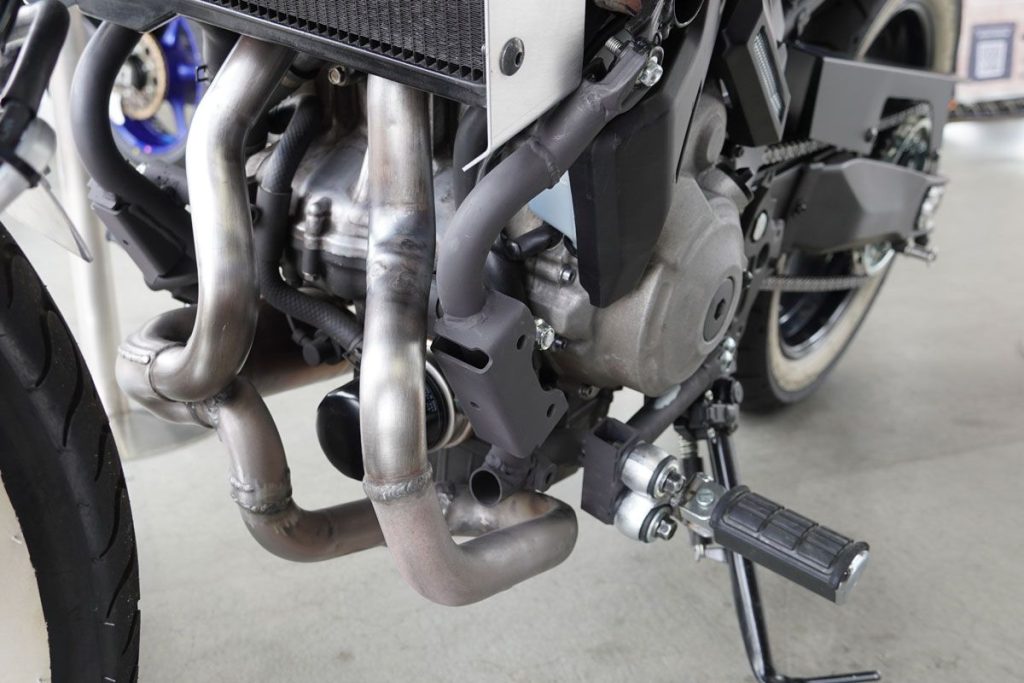 值得注意的是，右側排氣管比左側更長，這種略帶「拼接感」的造型，也正是概念提案車特有的風格。腳踏位置也被向前移動了，營造出更具巡航氣息的騎乘姿勢。